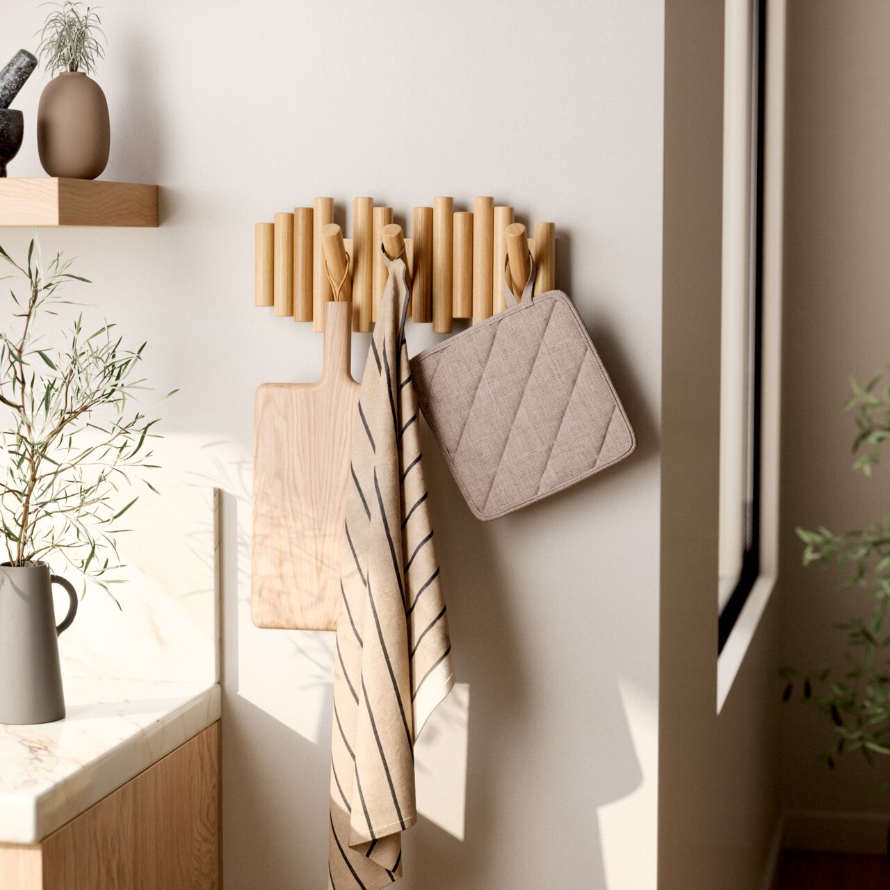 Moderne Wandgarderobe aus Holz mit mehreren Haken, an denen ein Schneidebrett, ein gestreiftes Handtuch und ein Topflappen hängen. Seitliche Perspektive.