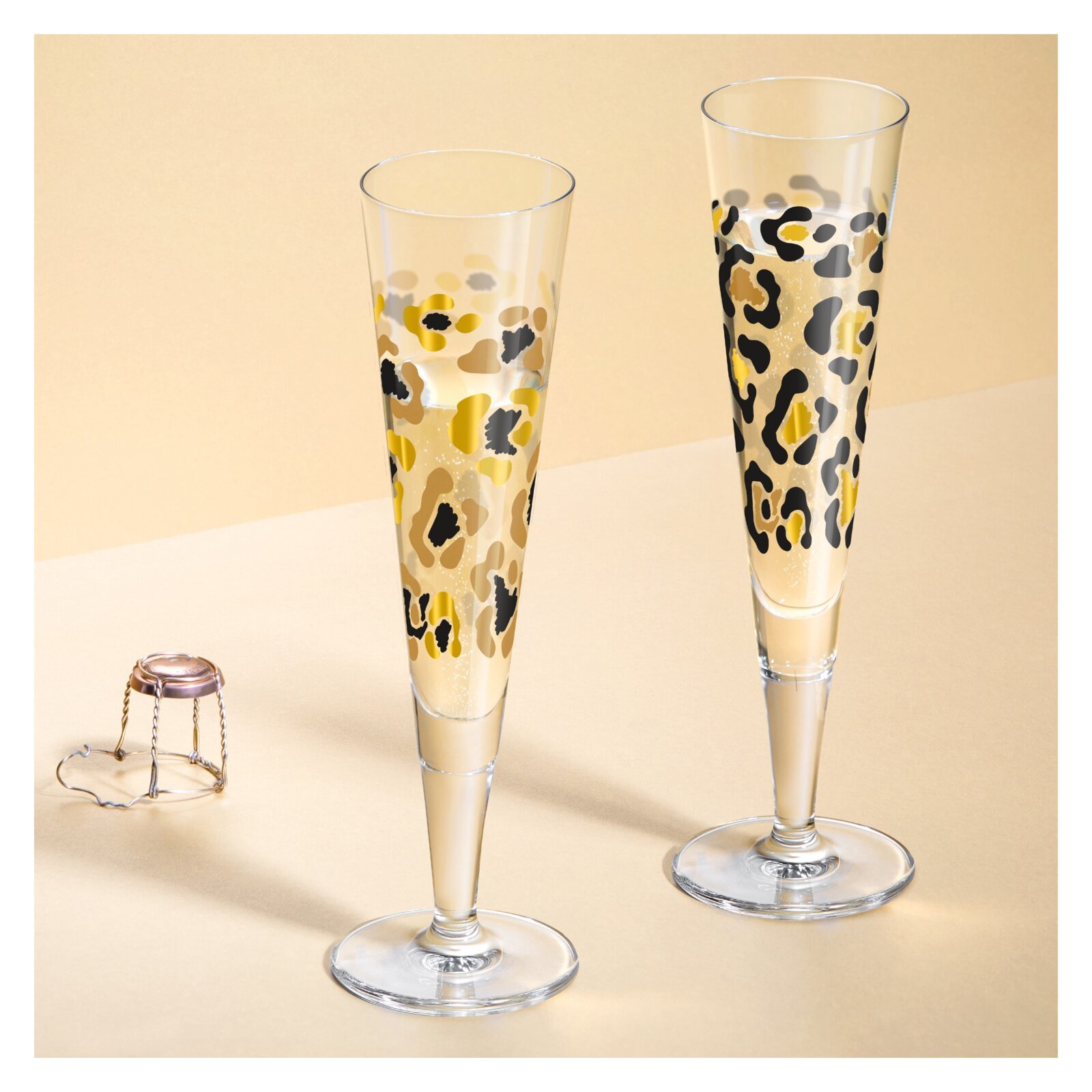 Zwei Champagnergläser mit Leopardenmuster, frontal fotografiert, auf einem beigen Hintergrund.