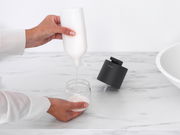 Seifenspender auf einer Marmoroberfläche, mit einer Hand, die Seife in ein Glasgefäß füllt. Perspektive von oben.