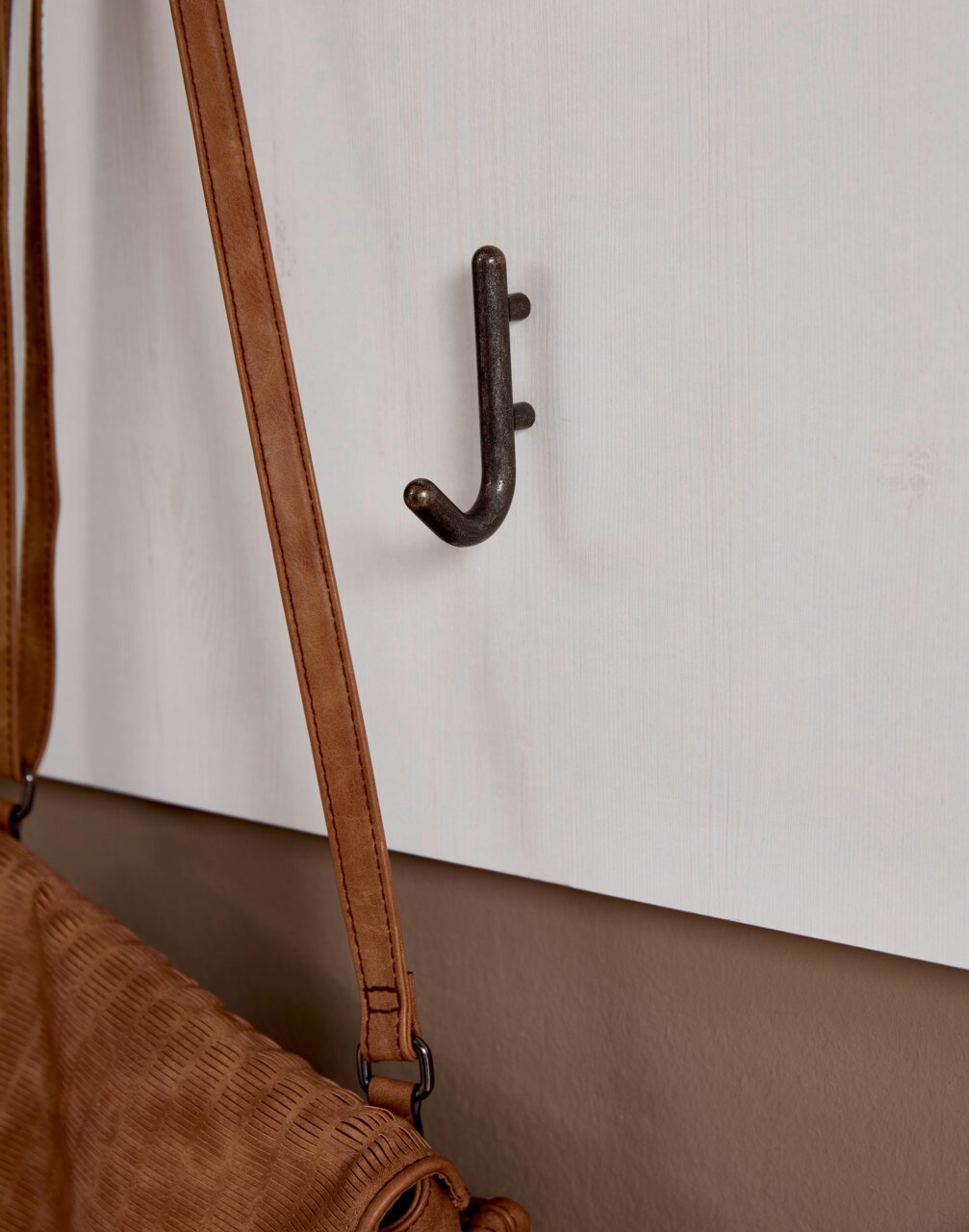 Nahaufnahme eines Garderobenhakens an einer weißen Wand, mit einer braunen Tasche daran hängend.