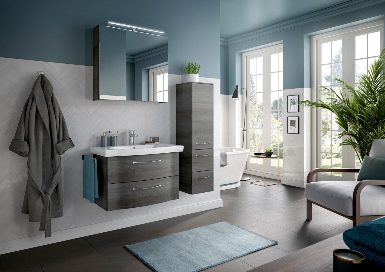 Moderne Badezimmermöbel in dunklem Holzton, bestehend aus einem Waschtisch mit zwei Schubladen und einem hohen Schrank, in einem stilvoll eingerichteten Badezimmer mit blauen Wänden und großen Fenstern, seitliche Perspektive.