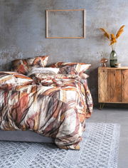 Bettwäsche-Set mit abstraktem Muster in warmen Erdtönen, auf einem grauen Bett in einem modern eingerichteten Raum mit Holzmöbeln und Dekorationen, aus seitlicher Perspektive fotografiert.