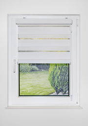 Doppelrollo mit Blende in der Größe 120x160cm, frontal an einem Fenster montiert, mit Blick auf einen grünen Garten.