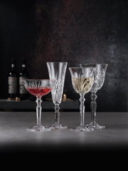 Vier elegante Kristallgläser, darunter ein Weißweinkelch, auf einer Tischoberfläche mit dunklem Hintergrund, seitliche Perspektive.