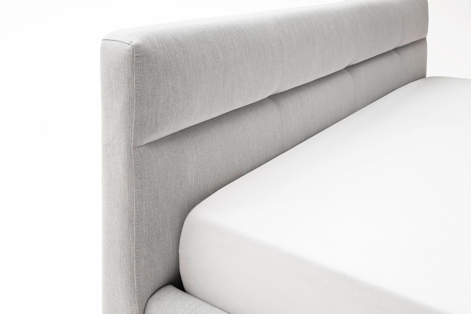 Nahaufnahme eines grauen Polsterbetts mit gepolstertem Kopfteil, seitliche Perspektive.