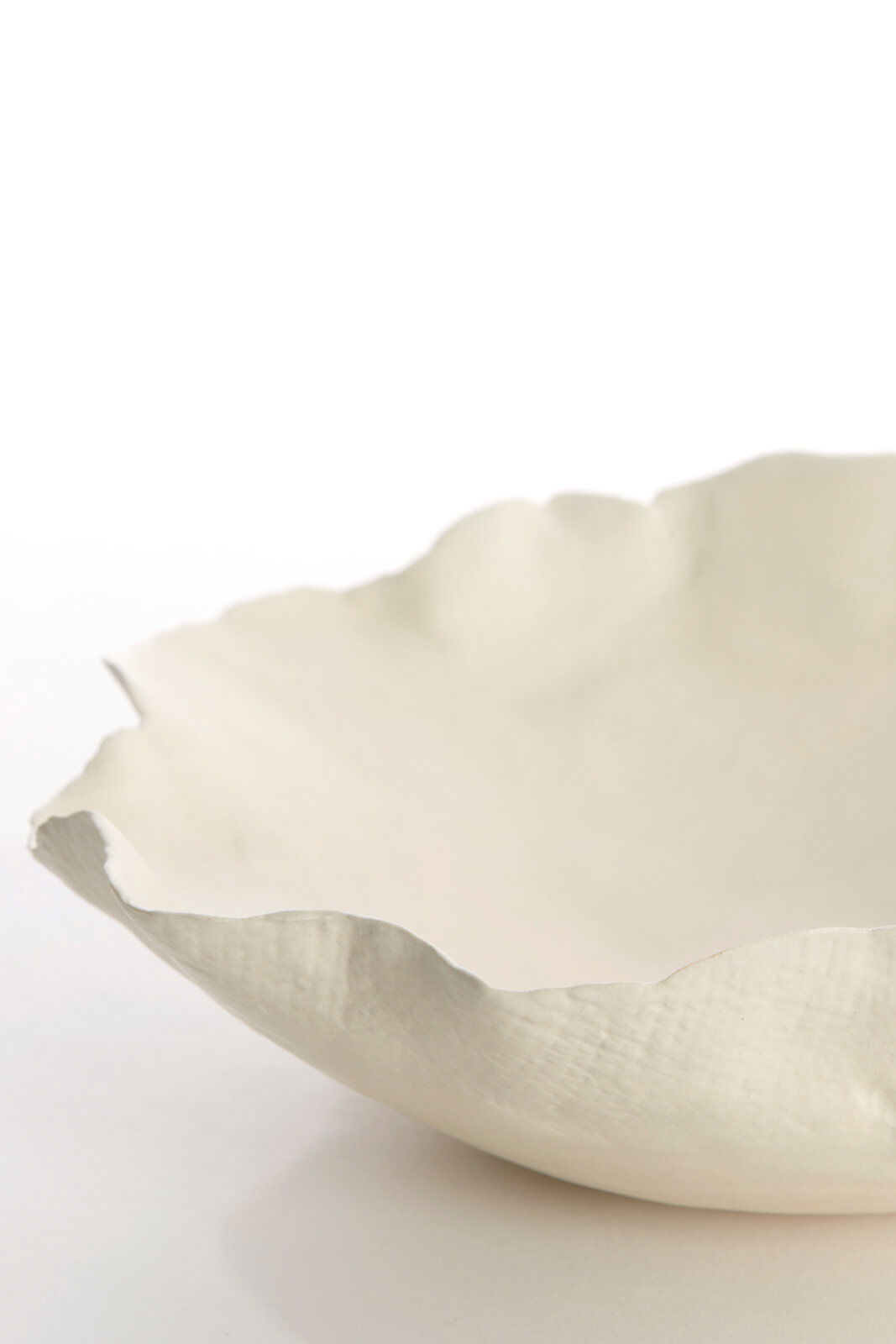 Nahaufnahme einer weißen, strukturierten Schale mit unregelmäßigem Rand, seitliche Perspektive.
