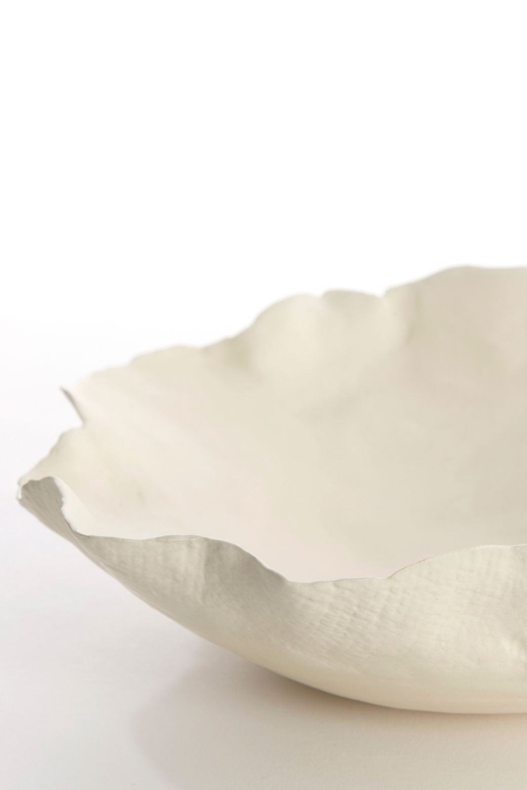 Nahaufnahme einer weißen, strukturierten Schale mit unregelmäßigem Rand, seitliche Perspektive.