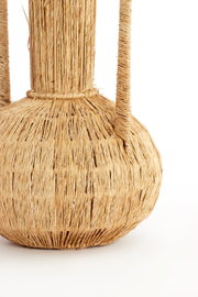 Close-up van een handgemaakte vaas van gevlochten natuurmateriaal met twee handvatten, zijaanzicht