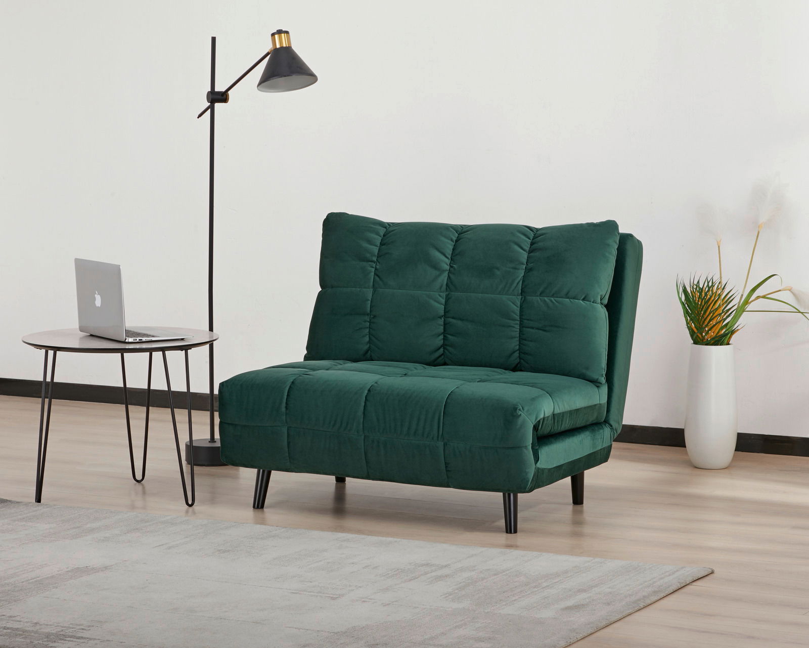 Grüner Funktionssessel in einem modernen Raum, seitliche Perspektive, neben einem runden Tisch mit Laptop und einer Stehlampe.