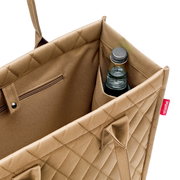 Nahaufnahme einer beigen Einkaufstasche mit Rautenmuster, die eine Flasche in einem Seitenfach zeigt. Perspektive von oben.