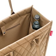 Nahaufnahme einer beigen Einkaufstasche mit Rautenmuster, die eine Flasche in einem Seitenfach zeigt. Perspektive von oben.