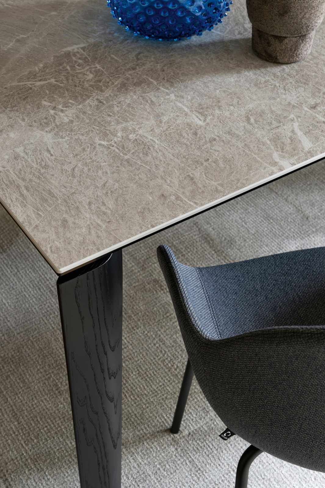 Connubia Esstisch BAND Nahaufnahme eines Connubia Esstisches BAND mit einer eleganten, marmorierten Tischplatte und einem schwarzen Tischbein. Perspektive von oben, ein Teil eines grauen Stuhls ist sichtbar.