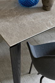 Nahaufnahme eines Connubia Esstisches BAND mit einer eleganten, marmorierten Tischplatte und einem schwarzen Tischbein. Perspektive von oben, ein Teil eines grauen Stuhls ist sichtbar.