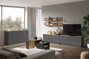 Moderne Wohnzimmermöbel in einem hellen Raum mit einem großen Fenster, bestehend aus einem grauen Sideboard, einem TV-Lowboard, einem Couchtisch und Wandregalen. Perspektive von vorne.