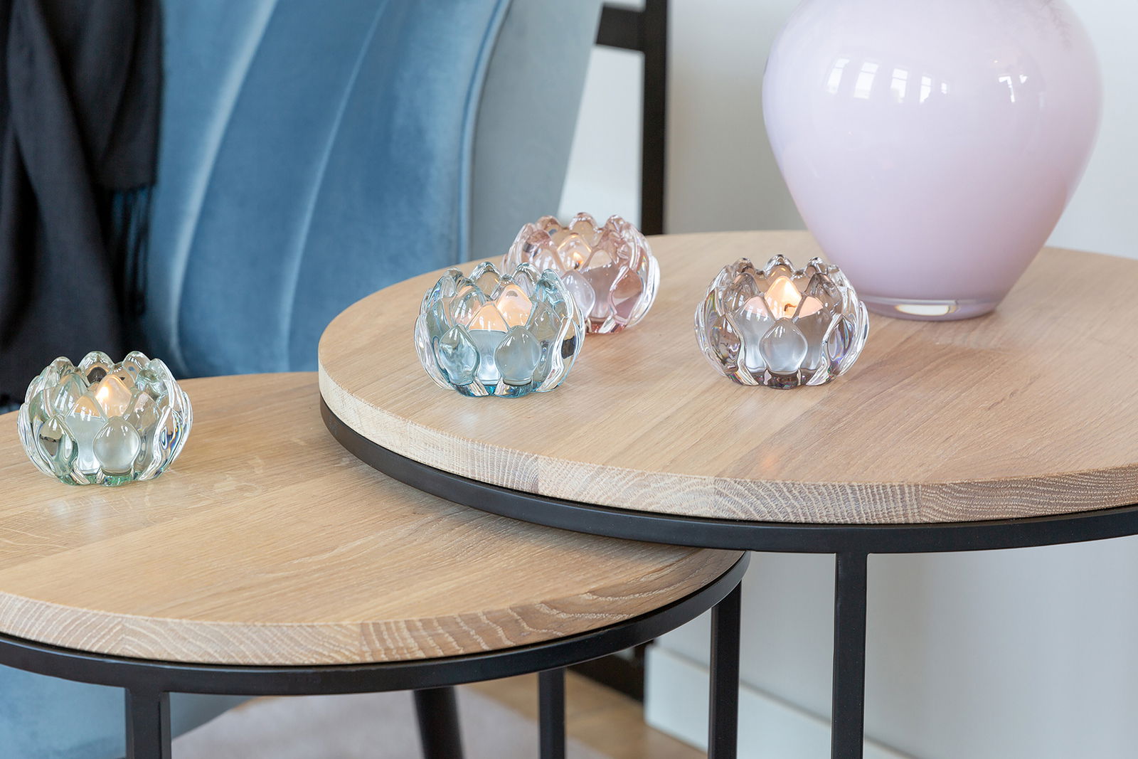 Vier LOTTA Teelichthalter aus Glas in verschiedenen Pastellfarben auf einem Holztisch, seitliche Perspektive.