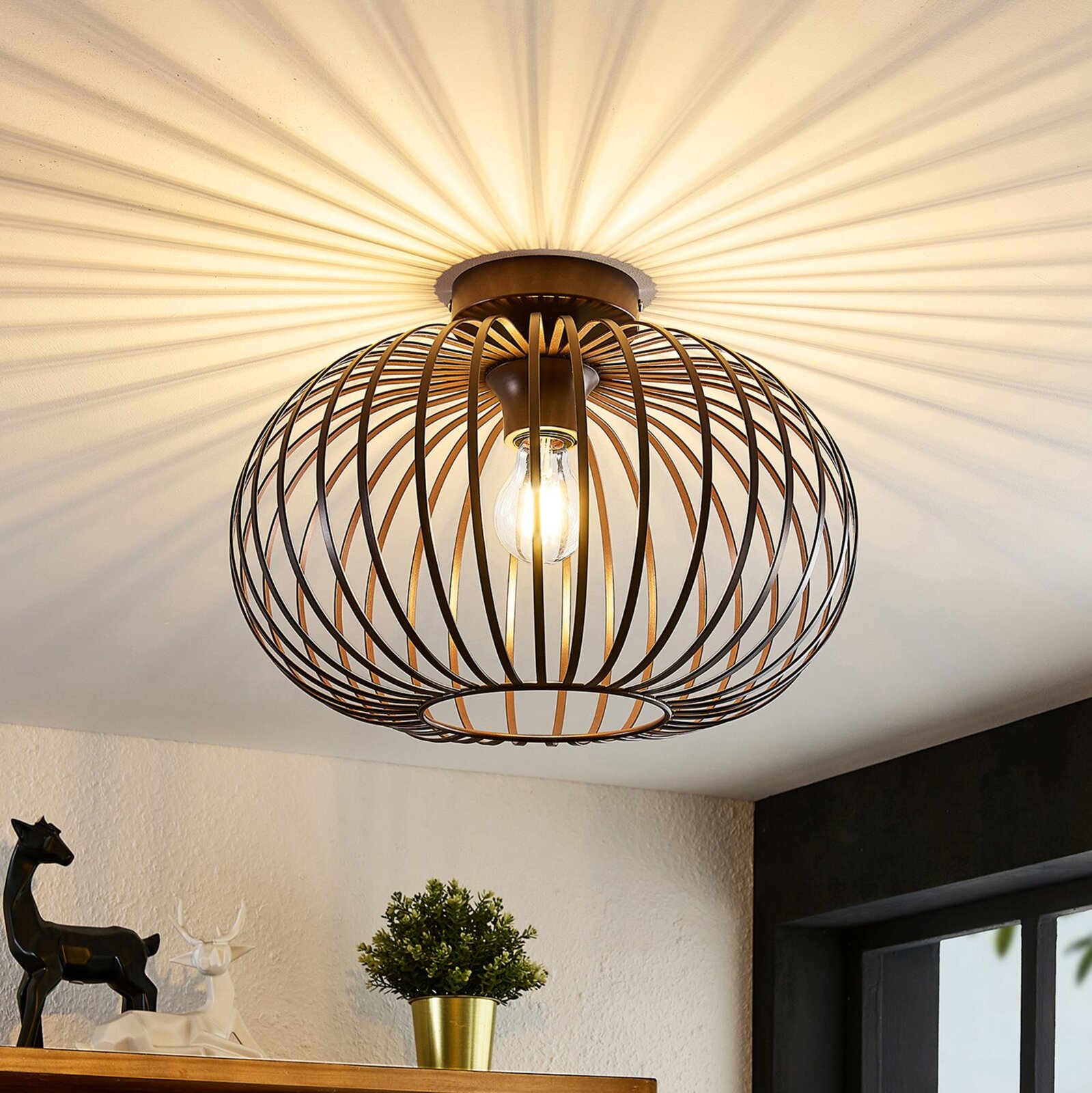 Moderne plafondlamp met een bolvormig, bronskleurig roosterontwerp, gefotografeerd van onderaf, die een warm licht op het plafond werpt.