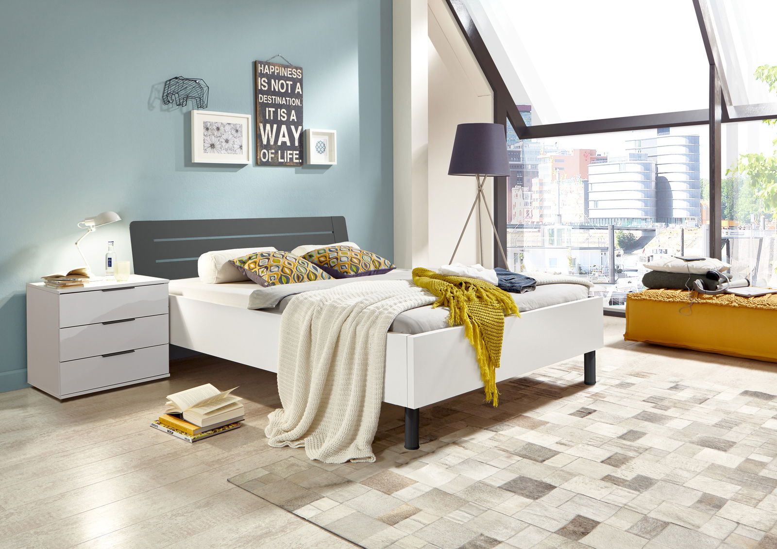 Modernes Futonbett in einem hellen Schlafzimmer mit großen Fenstern, seitliche Perspektive