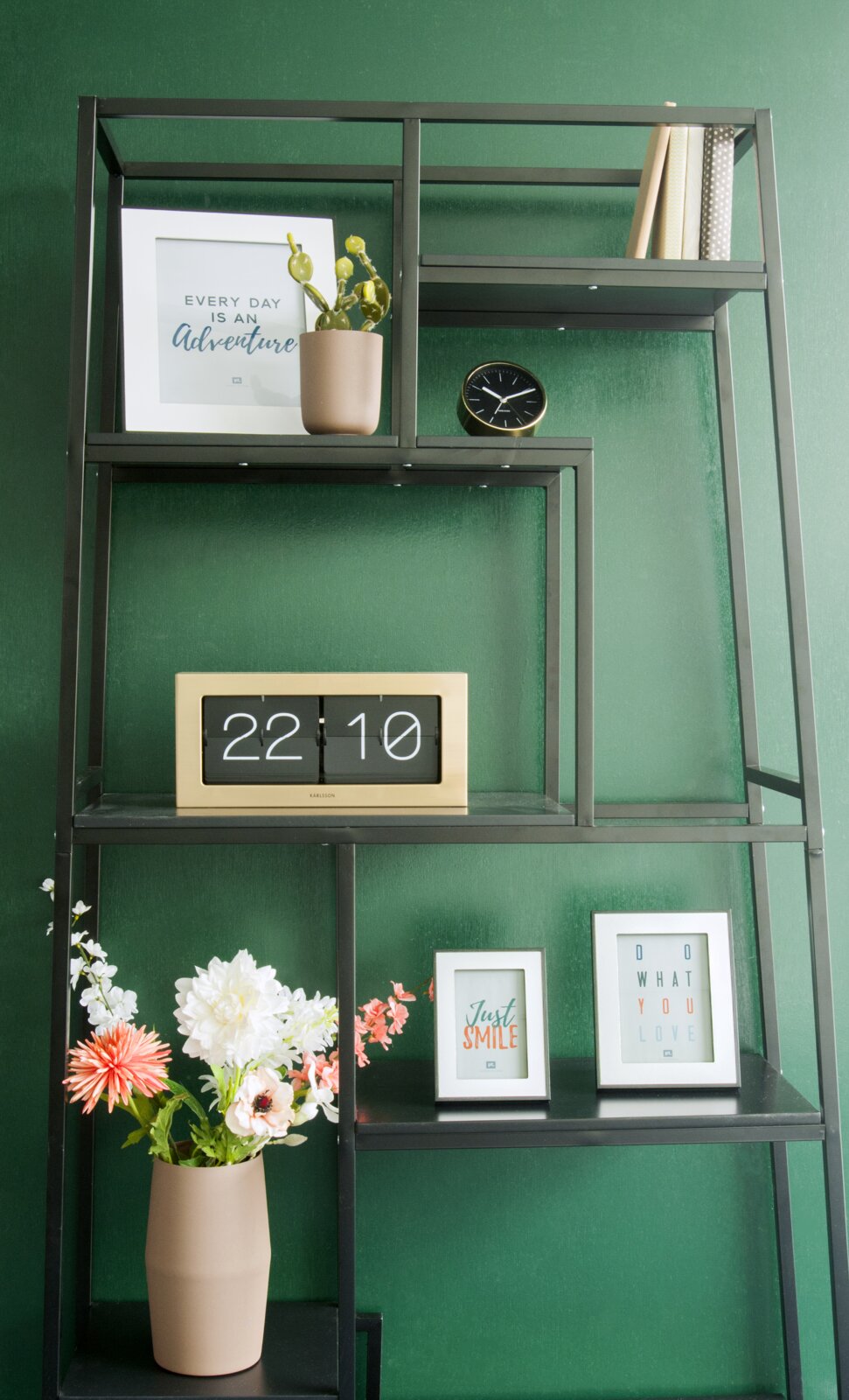 Een XL-tafelklok op een plank, omringd door decoraties zoals planten en fotolijstjes, gezien vanuit de voorkant.