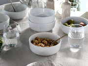 Weißes Kombiservice-Set mit Schalen und Gläsern auf einem gedeckten Tisch, seitliche Perspektive.