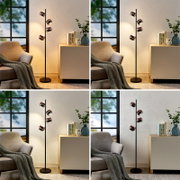 Moderne schwarze Stehleuchte mit vier kugelförmigen, kupferfarbenen Lampenschirmen neben Sessel und Sideboard im Wohnzimmer, frontale Perspektive