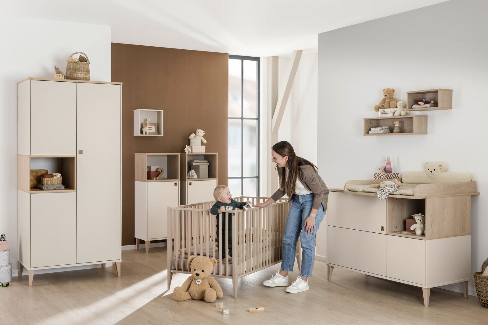 Kinderzimmer mit moderner Einrichtung, inklusive einer rechteckigen Wandbox an der Wand. Perspektive: seitliche Ansicht des Raumes mit einem Kleinkind im Gitterbett und einer Frau daneben.