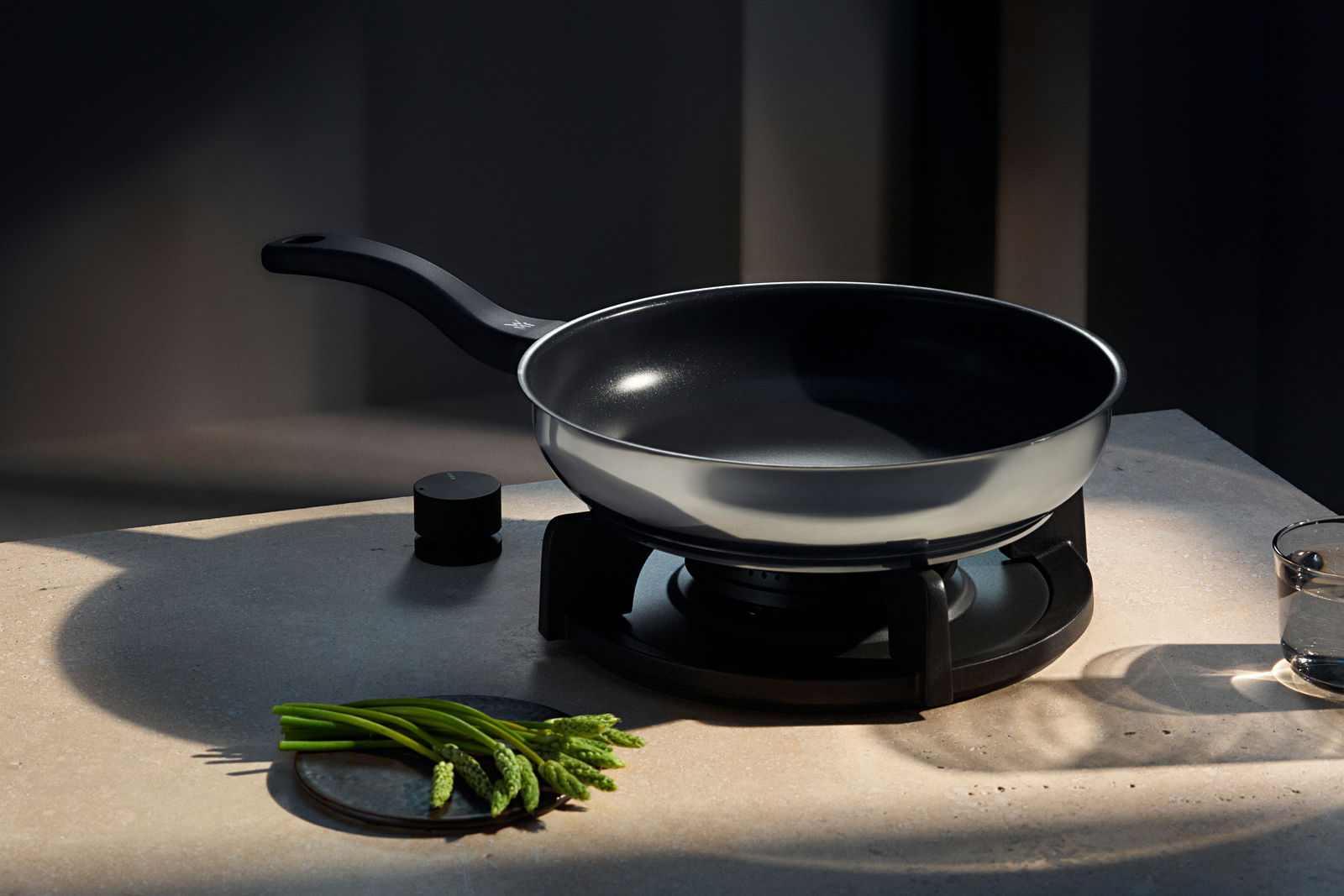 WMF Pfannen-Set 2-tlg. DEVIL Pfanne aus dem Pfannen-Set Devil, seitliche Perspektive auf einem Herd, mit schwarzem Griff und glänzender Oberfläche.