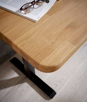 Eckansicht eines E-Schreibtischs mit heller Holzoberfläche und schwarzem Metallfuß, darauf liegen eine Brille und ein aufgeschlagenes Buch.