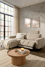 Beige Ecksofa mit verstellbarer Rückenlehne und Fußstütze, linksseitig, in einem modernen Wohnzimmer mit großen Fenstern und Holztisch, seitliche Perspektive