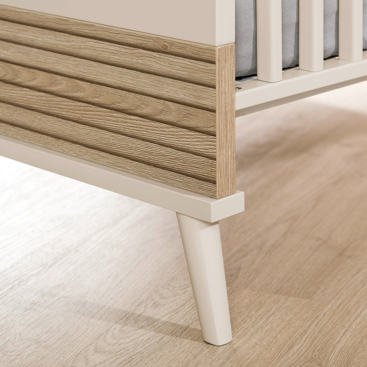 Detailfoto van een babybedje met houten bekleding en witte poten.