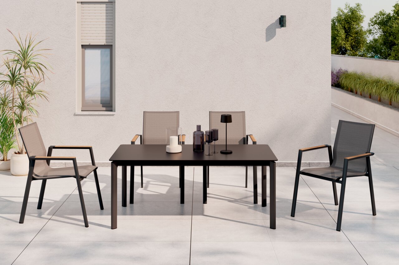 Moderner Stapelstuhl aus Metall und Textil mit Armlehnen, auf einer Terrasse neben einem Tisch, aus der Frontalperspektive.