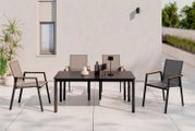 Moderner Stapelstuhl aus Metall und Textil mit Armlehnen, auf einer Terrasse neben einem Tisch, aus der Frontalperspektive.