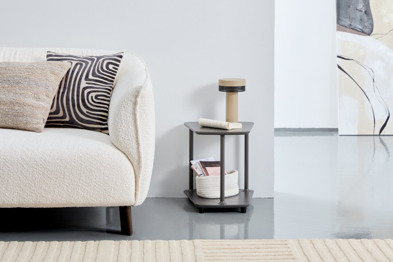 Moderner Beistelltisch XORA VIOLA in dunklem Grau, seitliche Perspektive, neben einem cremefarbenen Sofa mit dekorativen Kissen, auf einem hellen Teppichboden.