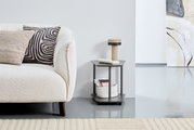Moderner Beistelltisch XORA VIOLA in dunklem Grau, seitliche Perspektive, neben einem cremefarbenen Sofa mit dekorativen Kissen, auf einem hellen Teppichboden.