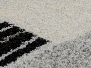 Nahaufnahme eines Frisé-Teppichs mit geometrischem Muster in Schwarz, Grau und Cremefarben. Die Perspektive zeigt die Textur und das Design des Teppichs aus der Nähe.