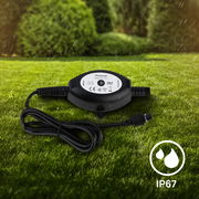 Dämmerungssensor mit IP67-Schutz, liegend auf einer Wiese, mit Kabel und Stecker, bei Regenwetter.