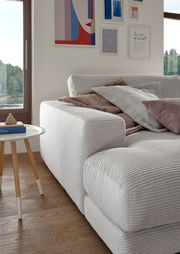 Nahaufnahme eines kleinen Megasofas in einem modernen Wohnzimmer, mit mehreren Kissen und einem Beistelltisch, aus seitlicher Perspektive.