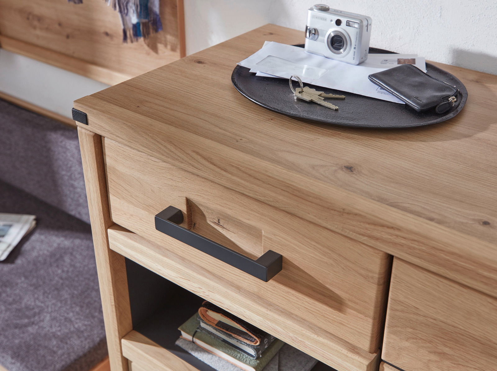 Nahaufnahme eines Schuhschranks aus Holz mit schwarzem Griff, darauf liegen ein Schlüsselbund, eine Kamera und Briefe.