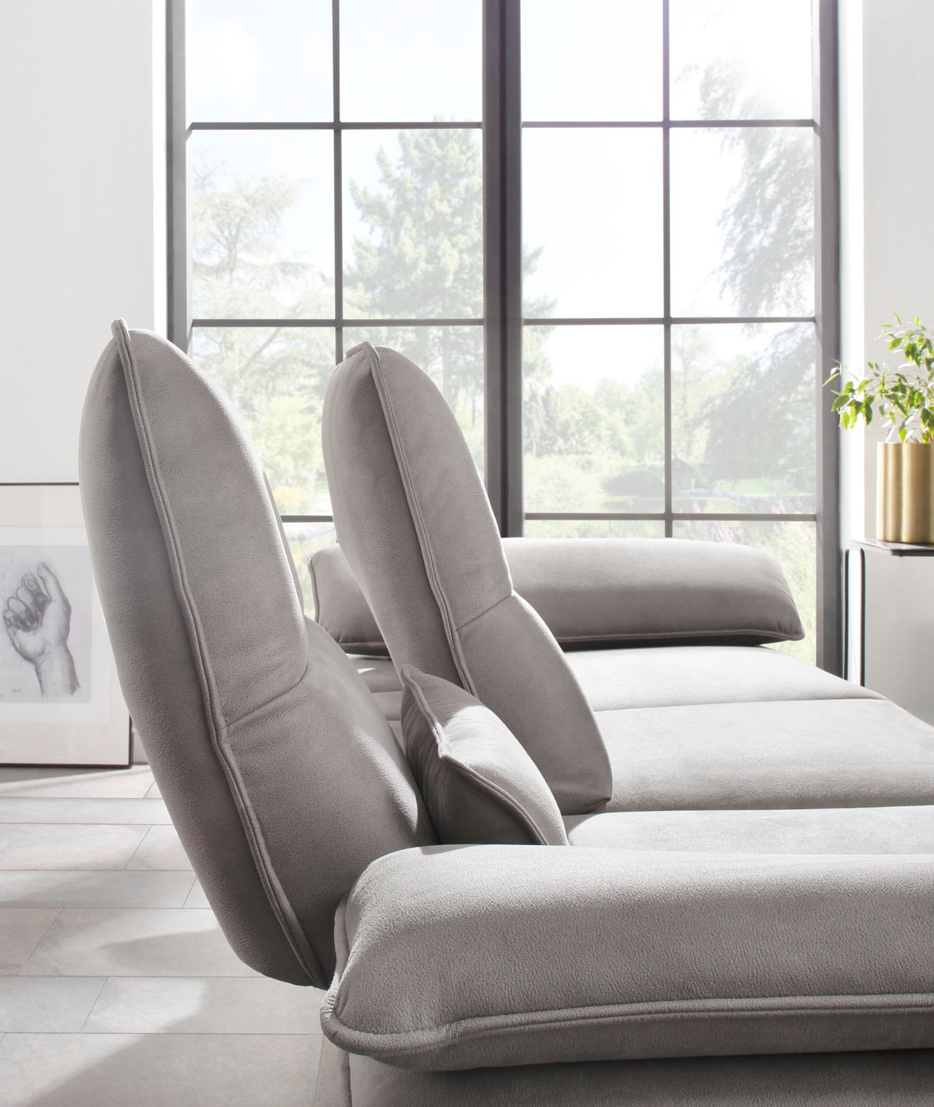 Graue Longchairkombination in einem modernen Wohnzimmer mit großen Fenstern, seitliche Perspektive.