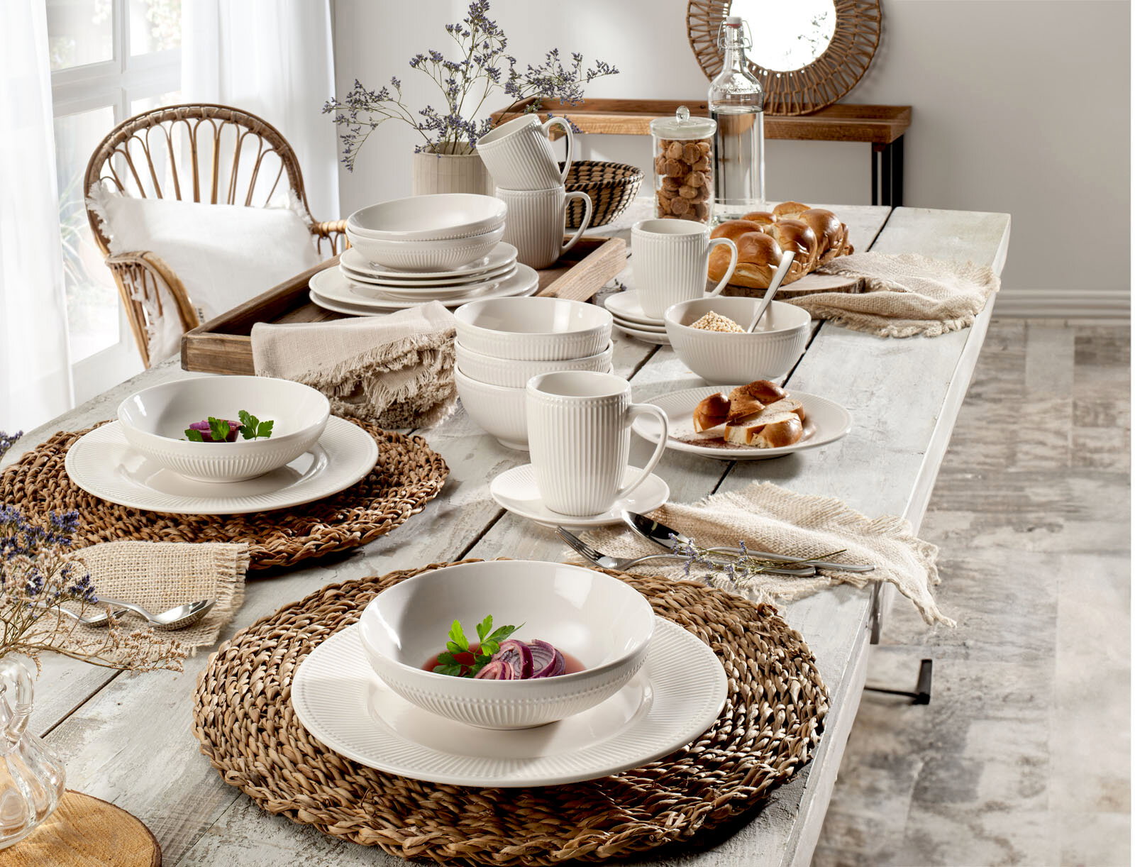 Ein stilvoll gedeckter Tisch mit dem 24-teiligen Kombiservice Nele, bestehend aus Tellern, Schalen und Tassen in einem eleganten, gerippten Design. Die Perspektive zeigt eine seitliche Ansicht des Tisches mit natürlicher Dekoration.