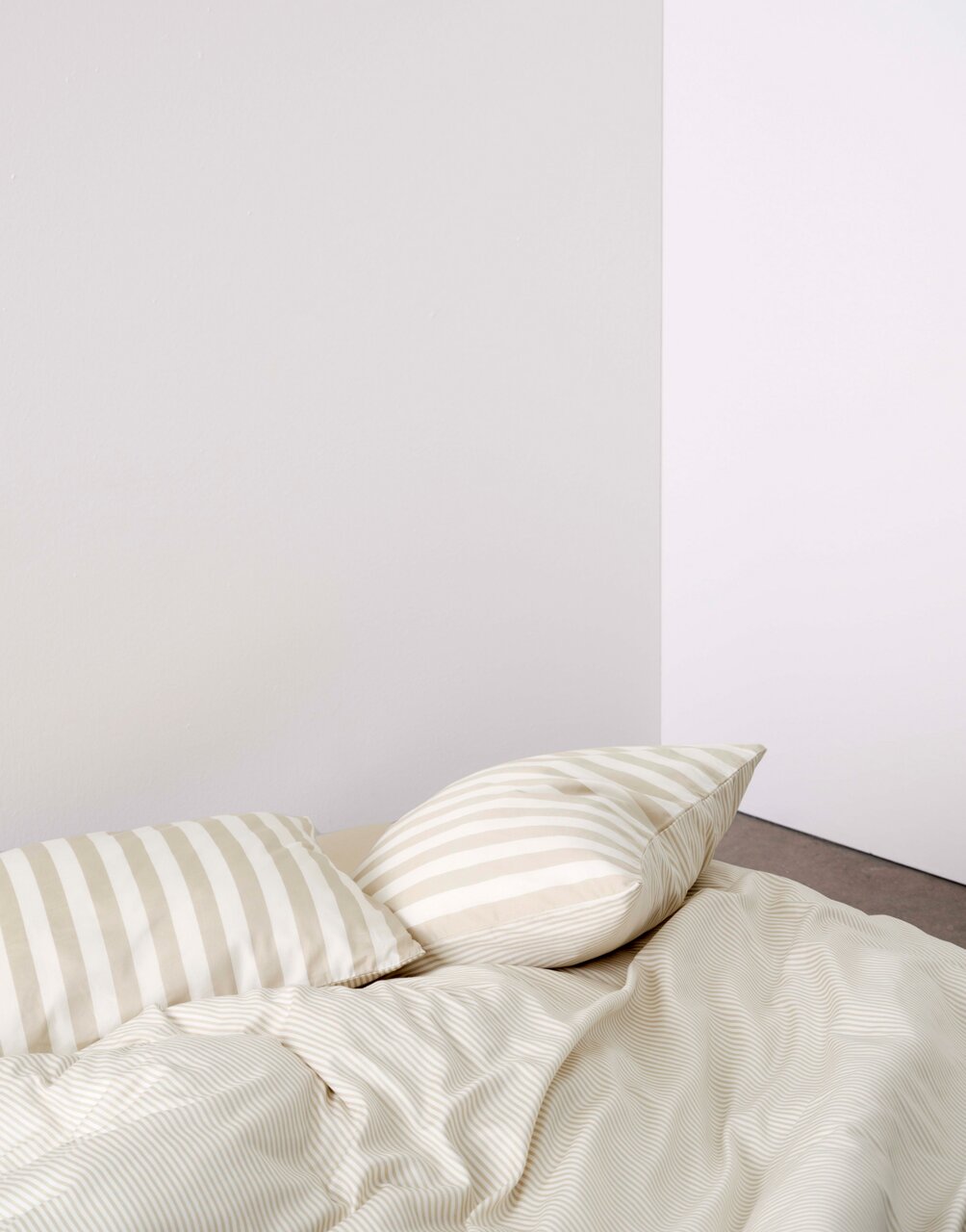 Bettwäsche-Set mit beigen und weißen Streifen, bestehend aus einem Kissenbezug und einer Bettdecke, aus der Perspektive von oben fotografiert.