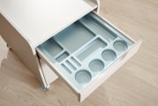 Weiße Rollkommode mit geöffneter Schublade und hellblauem, vielseitig unterteiltem Ordnungseinsatz, aus schräger Vogelperspektive betrachtet