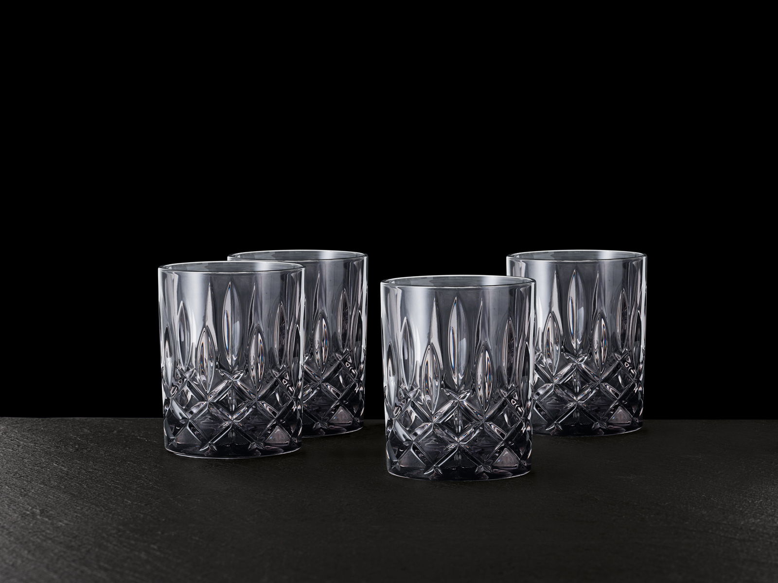 Vier elegante Whiskybecher mit Kristallschliff, frontal auf schwarzem Hintergrund präsentiert.