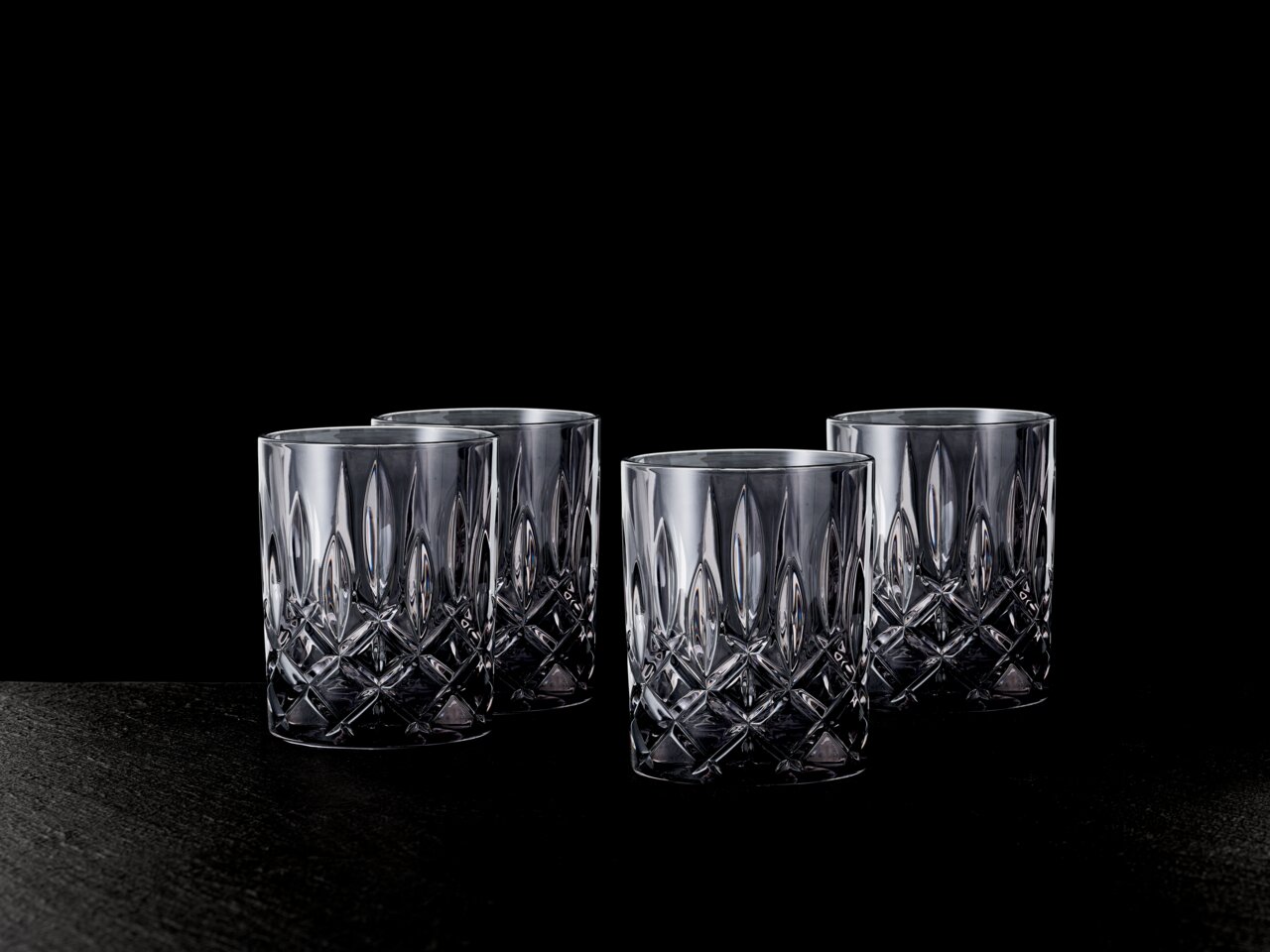 Vier elegante Whiskybecher mit Kristallschliff, frontal auf schwarzem Hintergrund präsentiert.