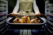 Eine Person nimmt eine Bratreine mit frisch gebackenen Brötchen aus dem Ofen. Die Perspektive ist von vorne auf die Bratreine gerichtet.