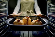 Eine Person nimmt eine Bratreine mit frisch gebackenen Brötchen aus dem Ofen. Die Perspektive ist von vorne auf die Bratreine gerichtet.