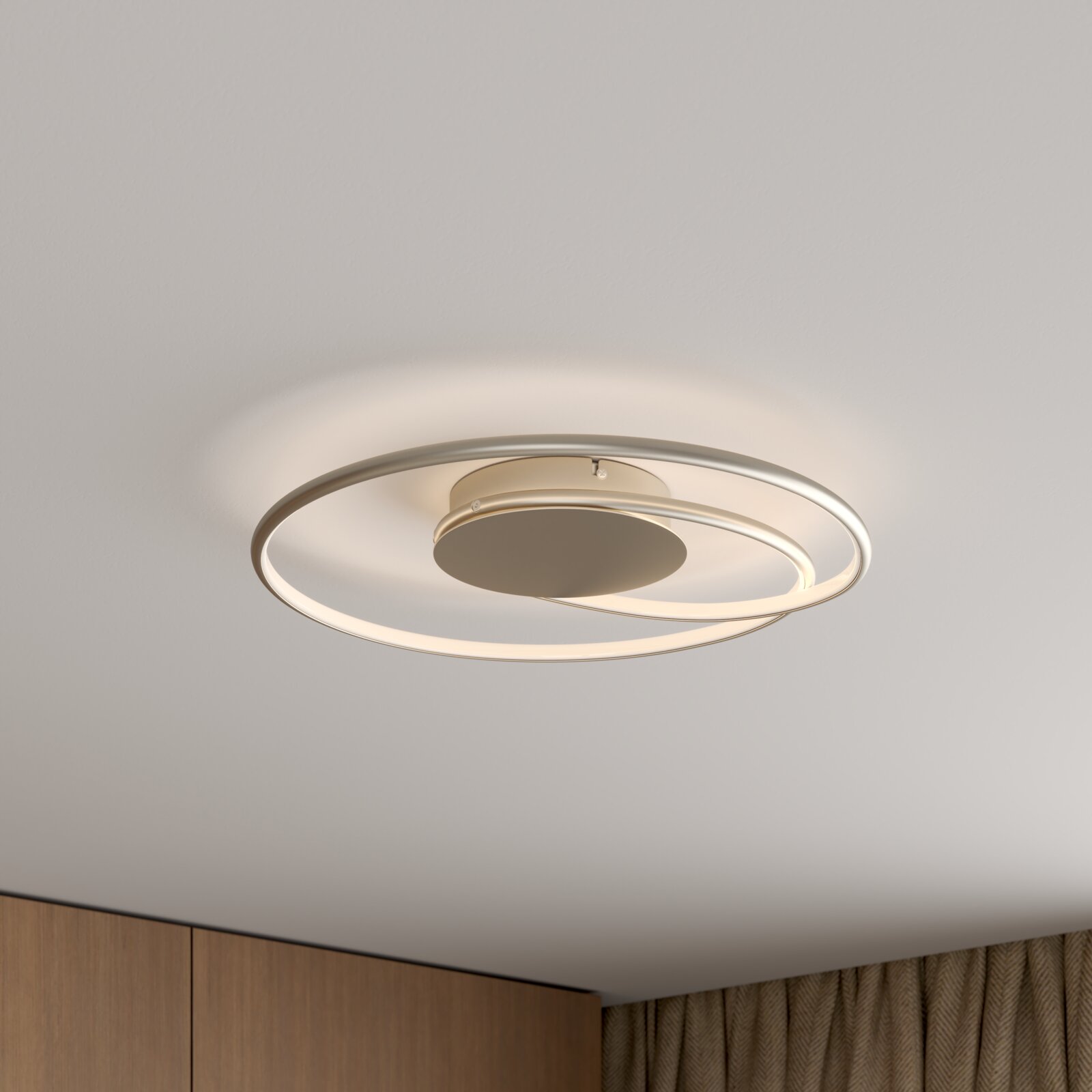 Moderne runde LED-Deckenleuchte mit zwei überlappenden Licht-Ringen in Silber/Champagner, warmweiß leuchtend, montiert an weißer Decke Perspektive: schräg von unten