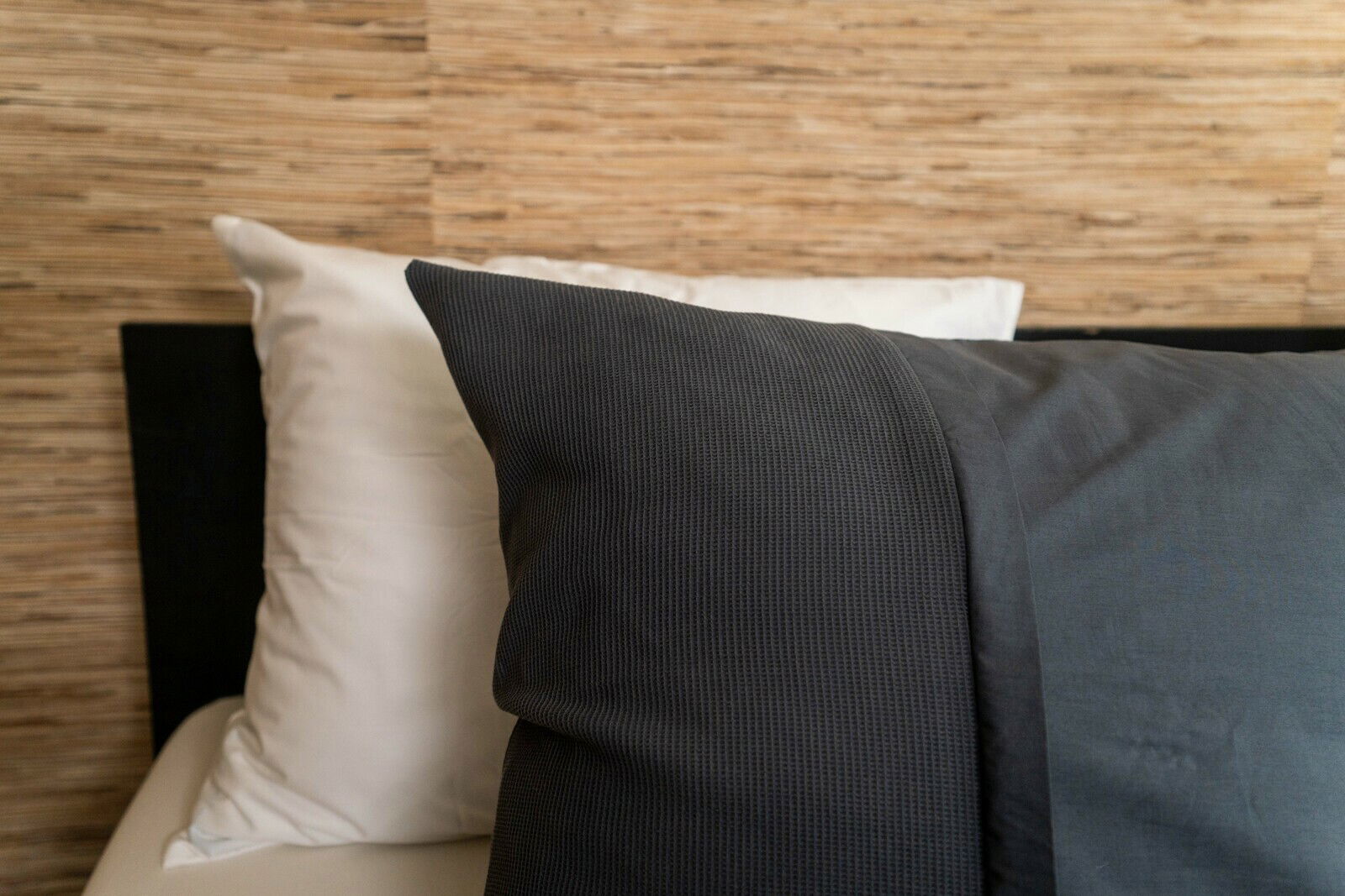 Nahaufnahme von Bettwäsche in dunklem Grau und Weiß auf einem Bett mit Holzrückwand.