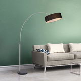 Moderne Stehleuchte mit gebogenem Arm und schwarzem Lampenschirm, neben einem grauen Sofa in einem Wohnzimmer mit grüner Wand, seitliche Perspektive