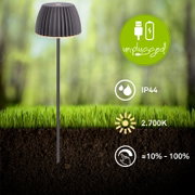Schwarze, kabellose LED-Gartenleuchte mit geriffeltem Schirm auf Erdspieß im Rasen, Vorderansicht leicht von oben; IP44, warmweiß 2700 K und dimmbar ca. 10–100%