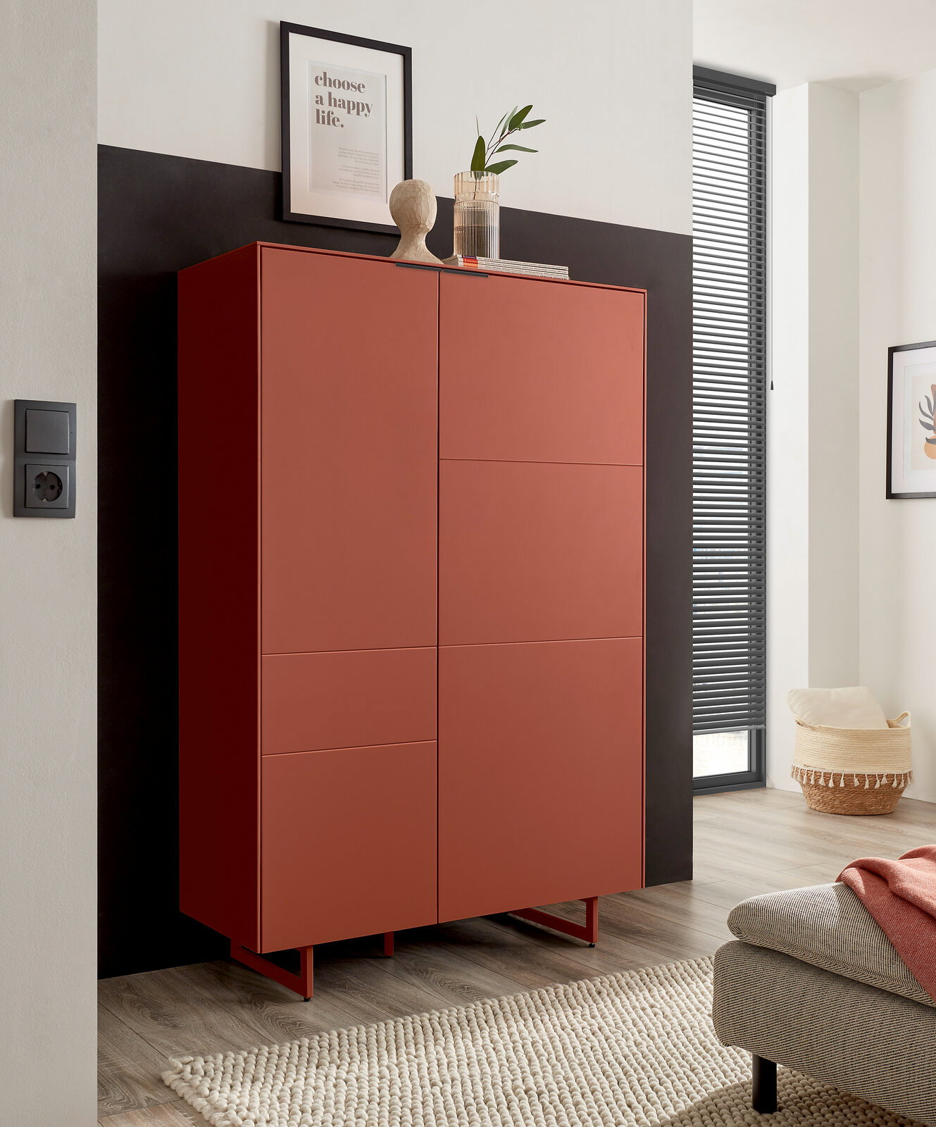Z2 Highboard QUODA Hoher, matt terrakottafarbener Schrank mit zwei Türen und schlanken Metallfüßen, in modernem Wohnraum vor dunkler Akzentwand – Frontansicht mit leichter Perspektive von links.
